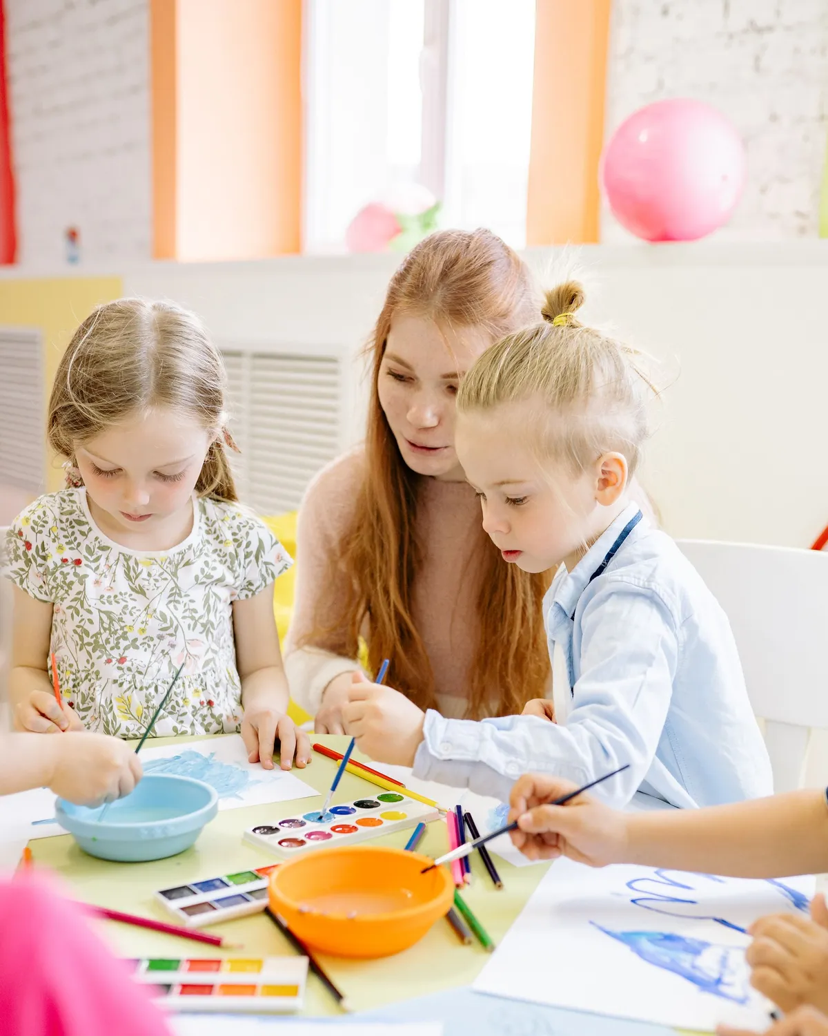 A teacher painting at a low table with young children