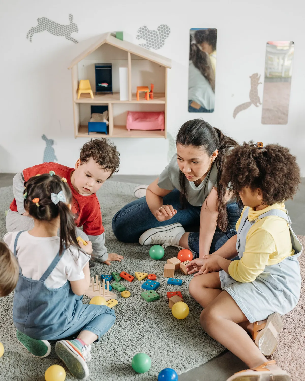 A teacher playing on the rug with young children in a bright preschool classroom