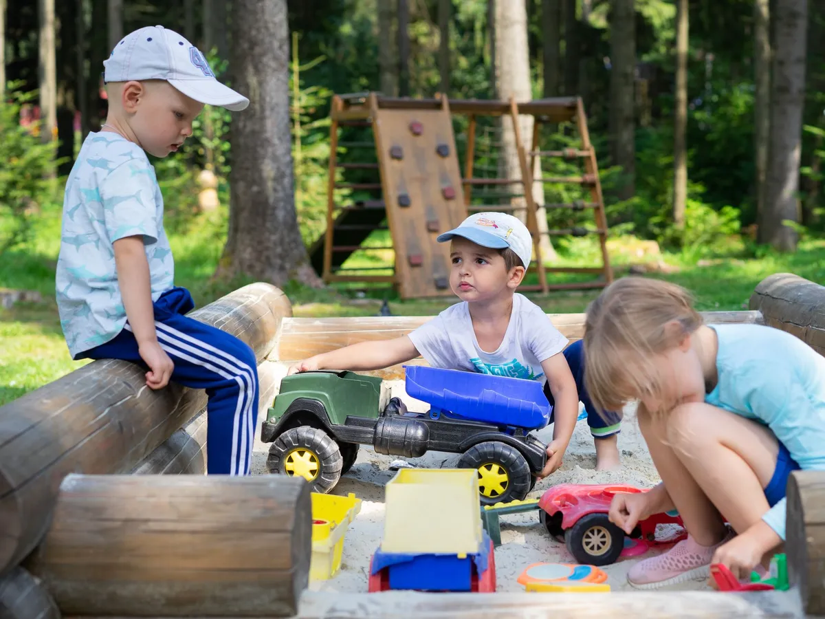 Children playing with toy trucks in a sandbox outdoors
