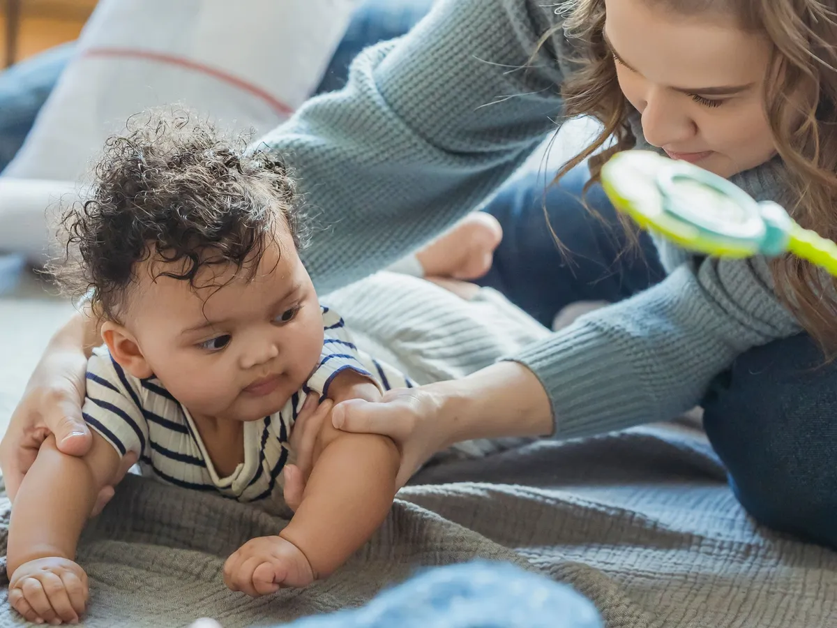 A caregiver playing with a baby during tummy time